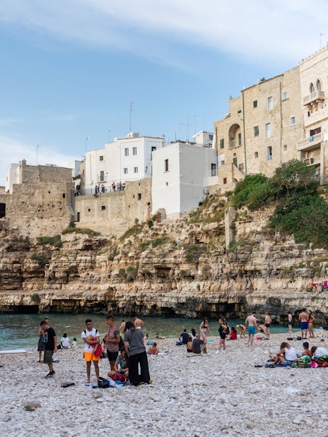 People enjoying Lama Monachile beach, surrounded by cliffs and historic buildings, Polignano a Mare, Italy.