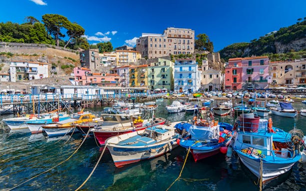 Colorful boats docked in Sorrento harbor with vibrant hillside buildings.