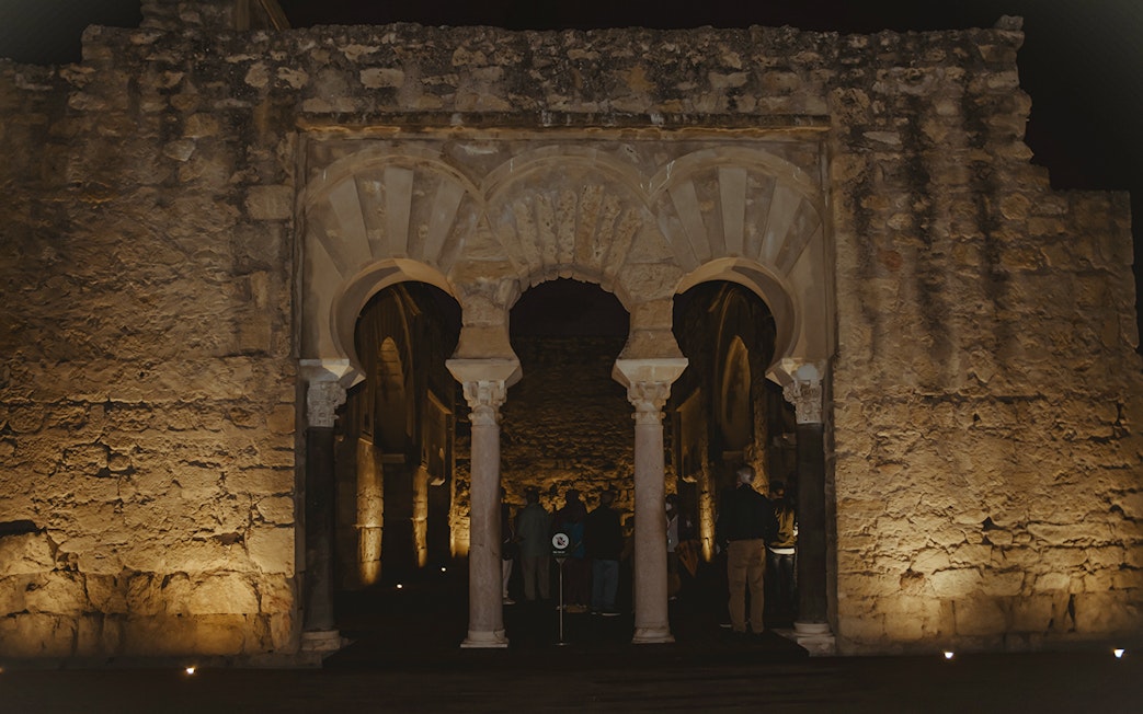 Guided group exploring illuminated arches of Medina Azahara at night.