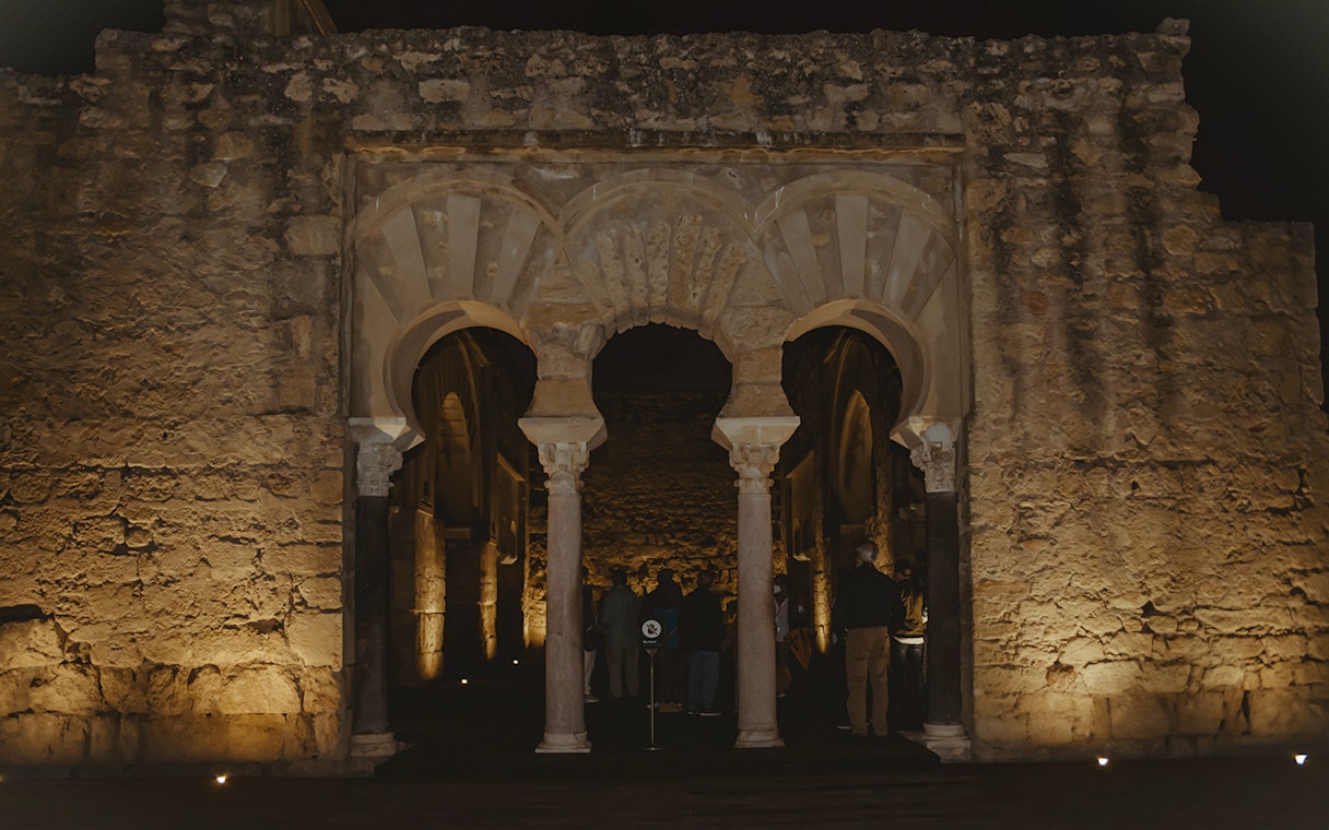 Guided group exploring illuminated arches of Medina Azahara at night.