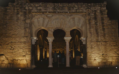 Guided group exploring illuminated arches of Medina Azahara at night.