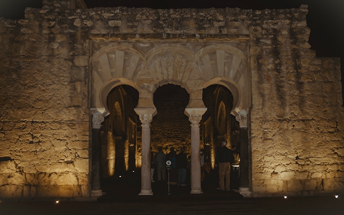 Guided group exploring illuminated arches of Medina Azahara at night.