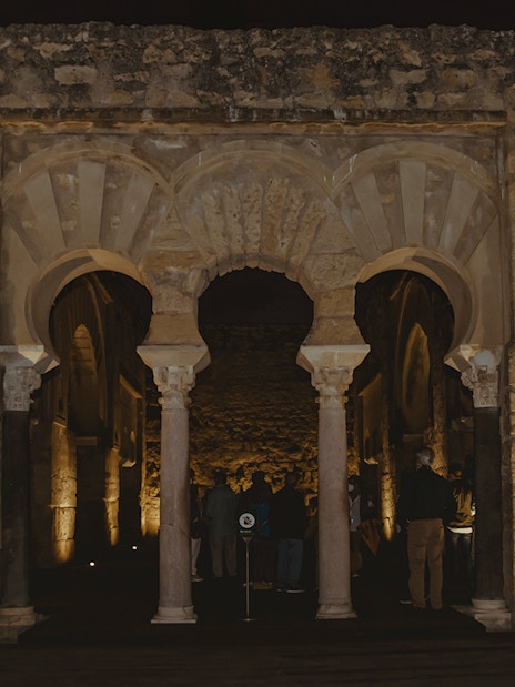 Guided group exploring illuminated arches of Medina Azahara at night.