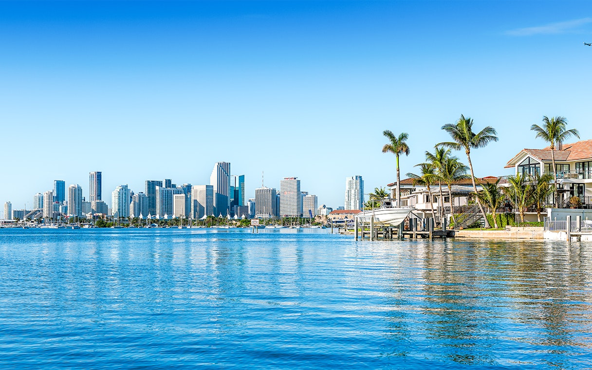 Skyline of Miami viewed from Biscayne Bay with waterfront homes and palm trees.