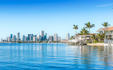 Skyline of Miami viewed from Biscayne Bay with waterfront homes and palm trees.