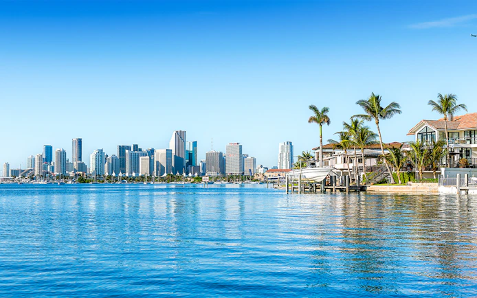 Skyline of Miami viewed from Biscayne Bay with waterfront homes and palm trees.