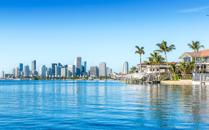 Skyline of Miami viewed from Biscayne Bay with waterfront homes and palm trees.