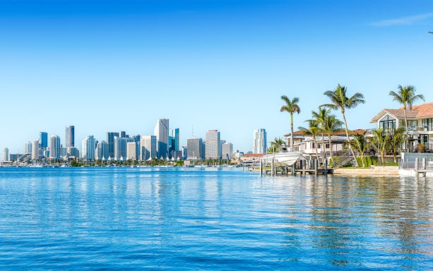 Skyline of Miami viewed from Biscayne Bay with waterfront homes and palm trees.