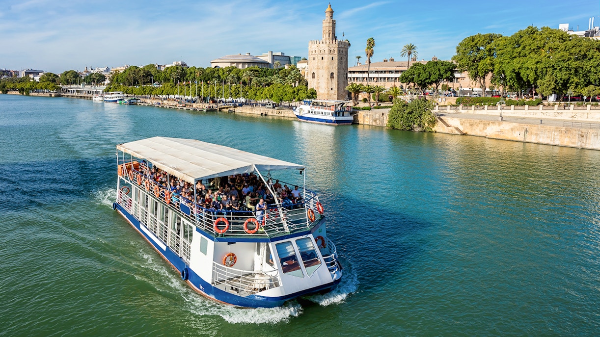 Tour boat cruising on the Guadalquivir River with Torre del Oro in Seville, Spain.