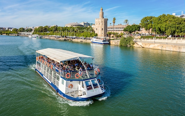 Tour boat cruising on the Guadalquivir River with Torre del Oro in Seville, Spain.