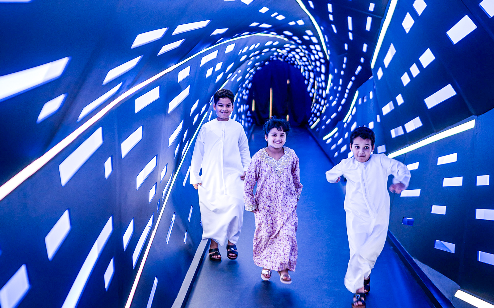 Children walking through an illuminated tunnel at Louvre Abu Dhabi.