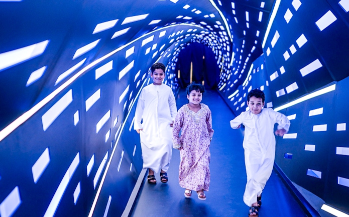 Children walking through an illuminated tunnel at Louvre Abu Dhabi.