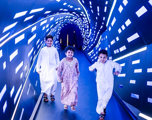 Children walking through an illuminated tunnel at Louvre Abu Dhabi.