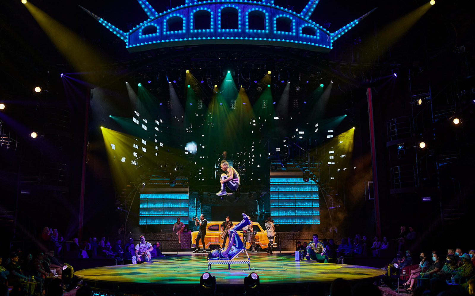 Acrobats performing on stage at Mad Apple show with vibrant cityscape backdrop.