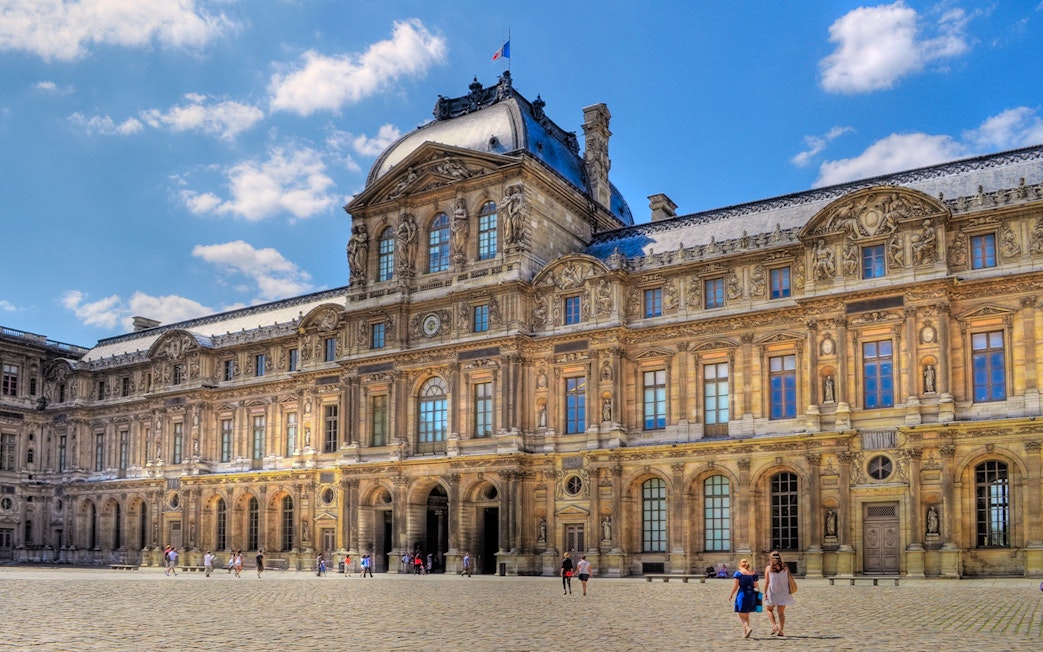 Louvre Museum courtyard with visitors walking on cobblestone.