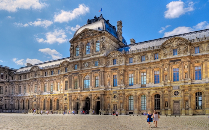 Louvre Museum courtyard with visitors walking on cobblestone.
