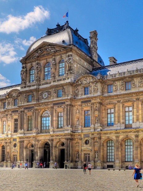 Louvre Museum courtyard with visitors walking on cobblestone.
