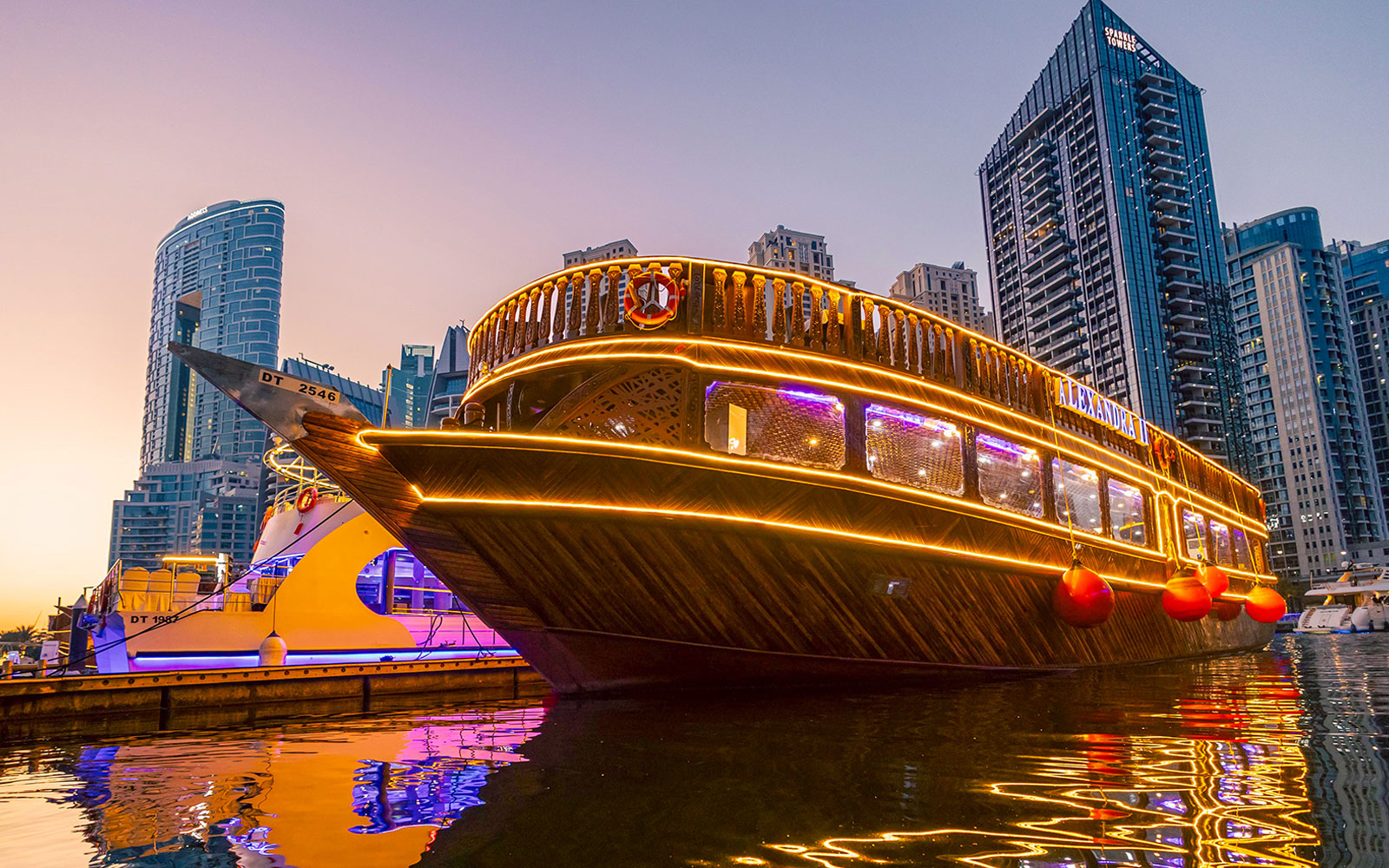 Alexandra Dhow Cruise illuminated at Dubai Marina during sunset.