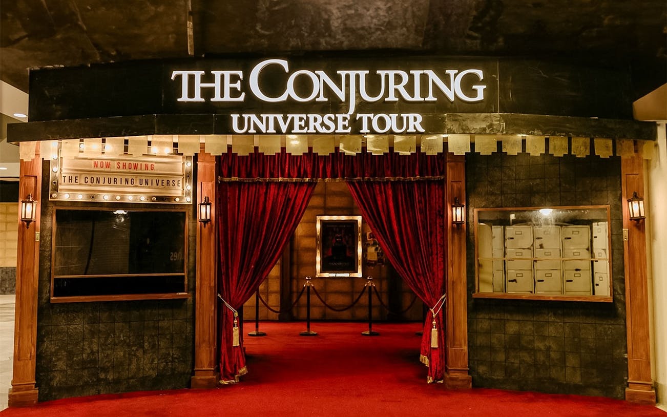 Entrance to The Conjuring Universe Tour in Malaysia with red curtains and marquee sign.