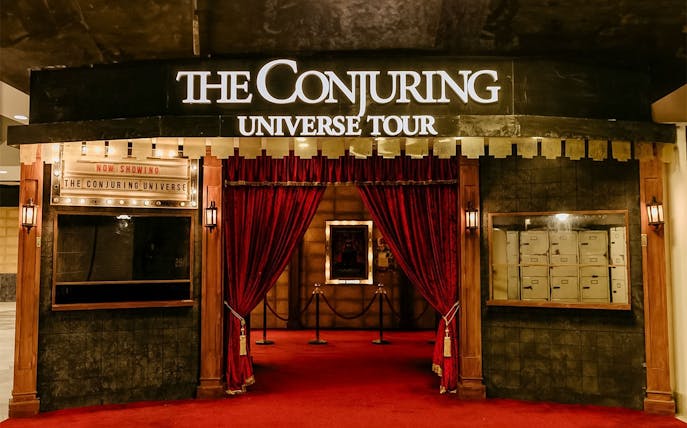 Entrance to The Conjuring Universe Tour in Malaysia with red curtains and marquee sign.