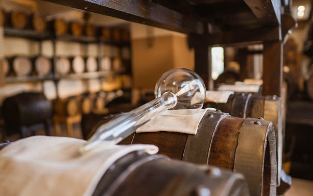 Vinegar barrels with glass siphon in a cellar during guided tasting tour.