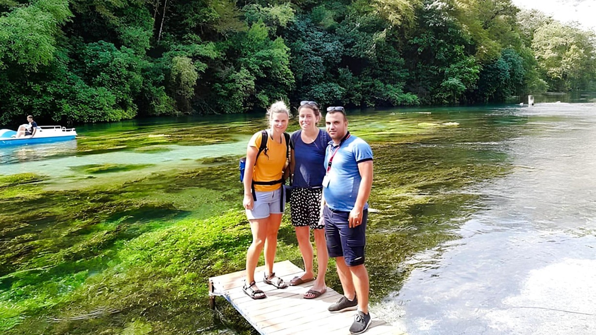 Guests standing on a wooden platform at Blue Eye springs, Albania, with lush greenery and clear water.