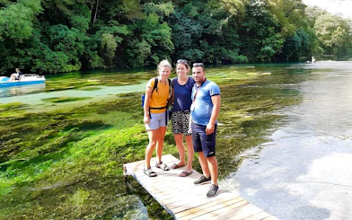 Guests standing on a wooden platform at Blue Eye springs, Albania, with lush greenery and clear water.