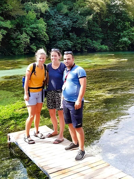 Guests standing on a wooden platform at Blue Eye springs, Albania, with lush greenery and clear water.