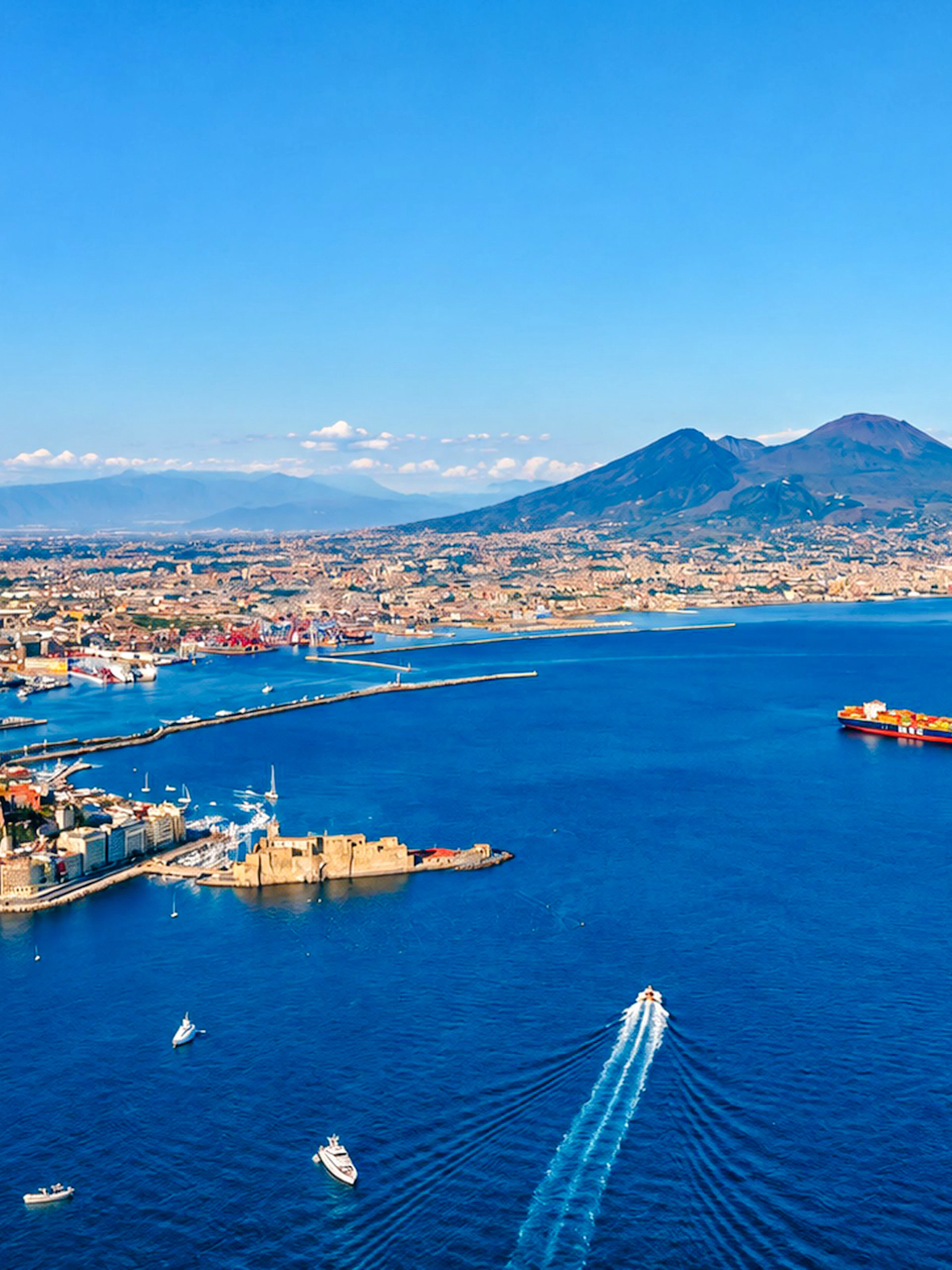 Aerial view of Naples coastline with boats heading towards Capri, featuring Mount Vesuvius in the background.