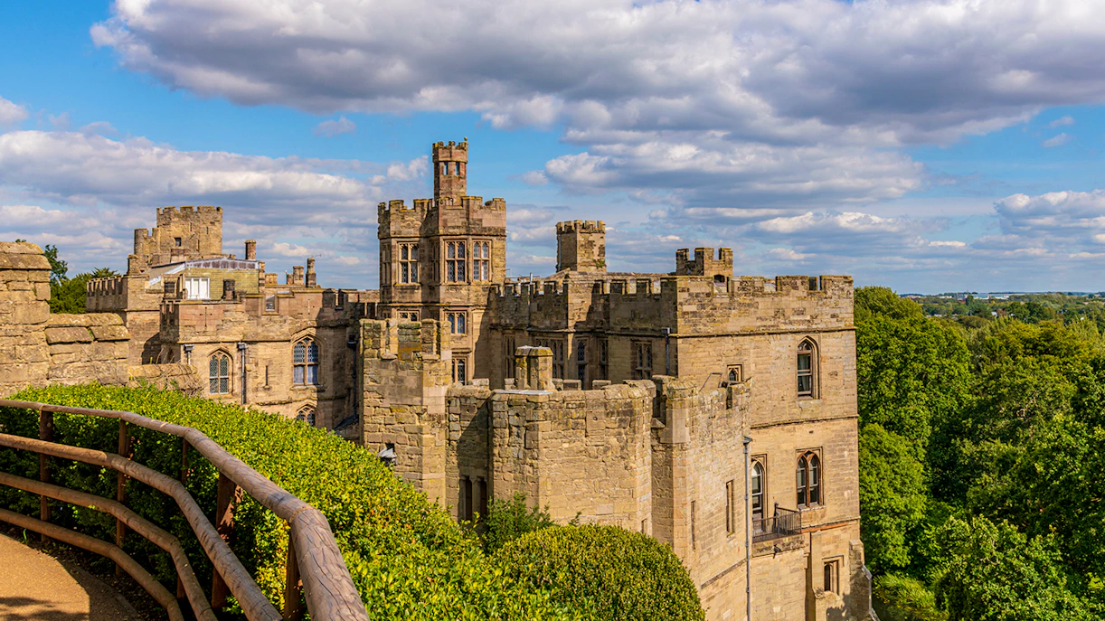 Warwick Castle towers overlooking lush greenery and distant landscape.