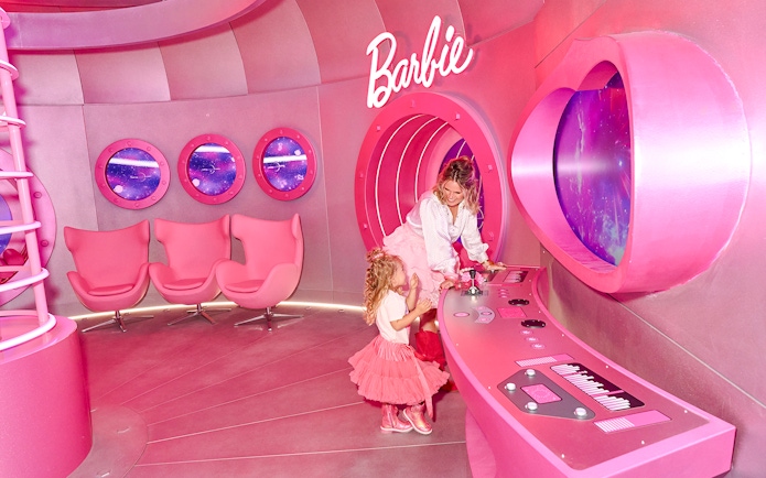 Guests exploring the pink Barbie rocketship interior with control panels and space-themed windows.