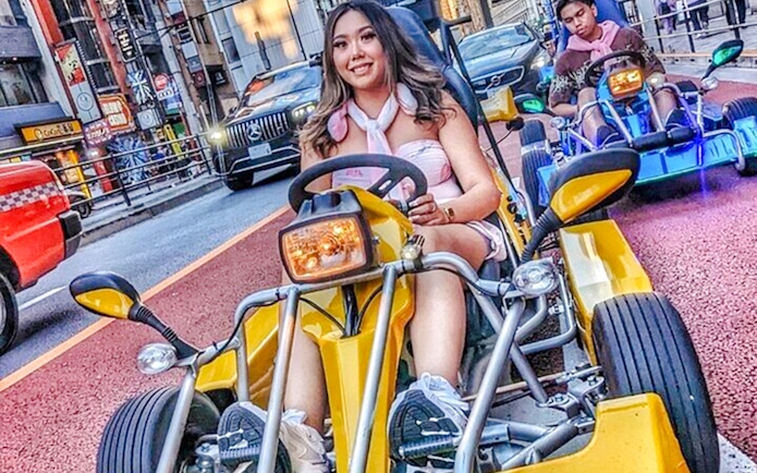 Woman in pink outfit driving a yellow go-kart on a Tokyo street.