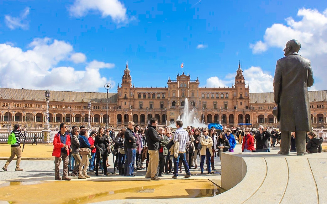 Group of tourists at Spain Square, Seville, with a guide near a fountain and historic building.
