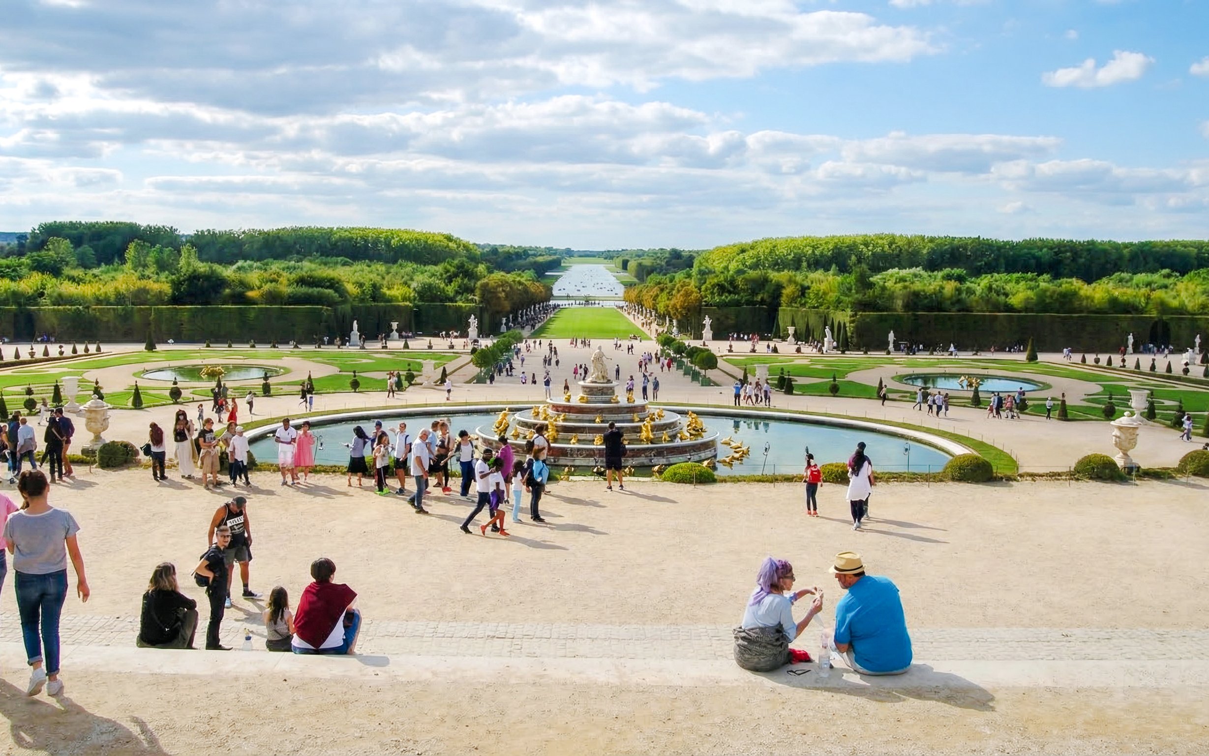 Visitors exploring the gardens and fountains at the Palace of Versailles, France.