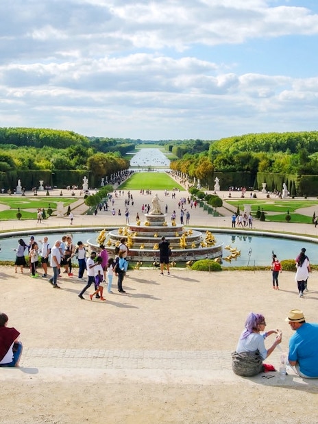 Visitors exploring the gardens and fountains at the Palace of Versailles, France.