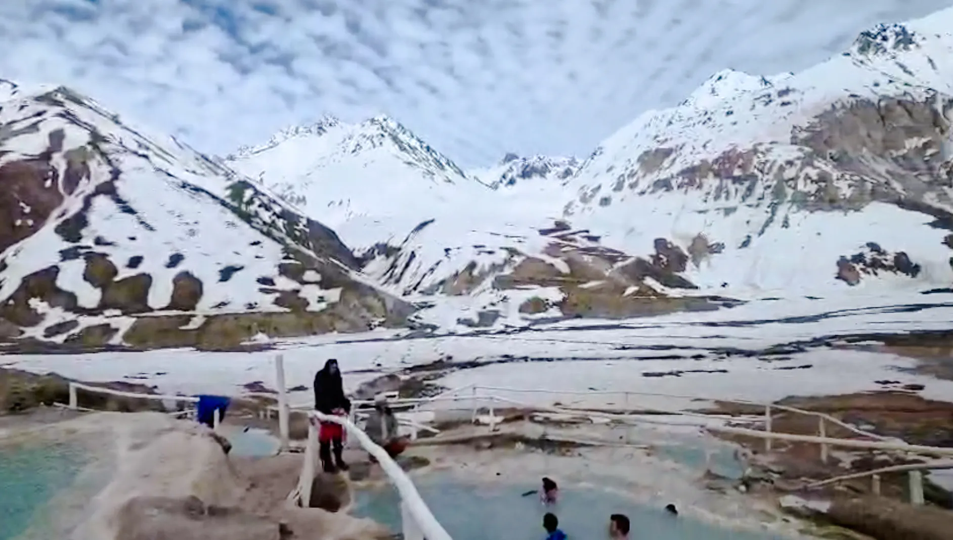 Visitors enjoying hot springs at Termas Baños Colina with snow-covered Andes in Cajon del Maipo, Santiago.