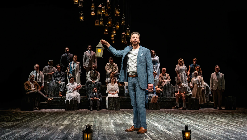 Stage performance of "Our Town" with actors holding lanterns.