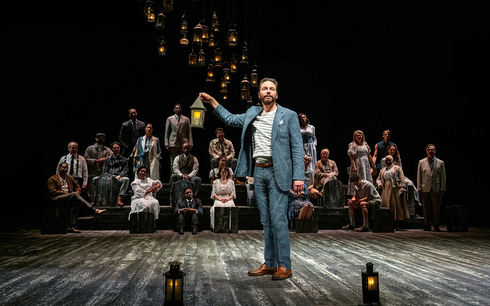 Stage performance of "Our Town" with actors holding lanterns.