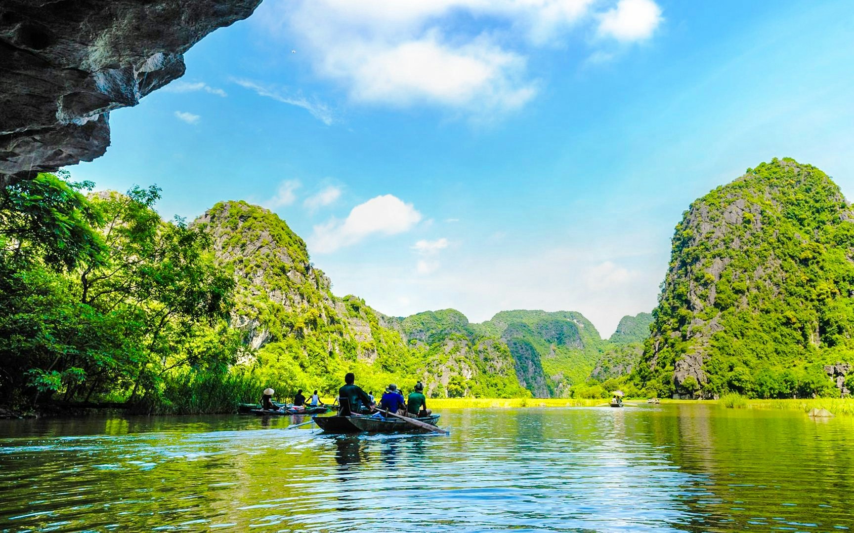Boat tour through Tam Coc rice fields with limestone karsts in the background, Ninh Binh, Vietnam.