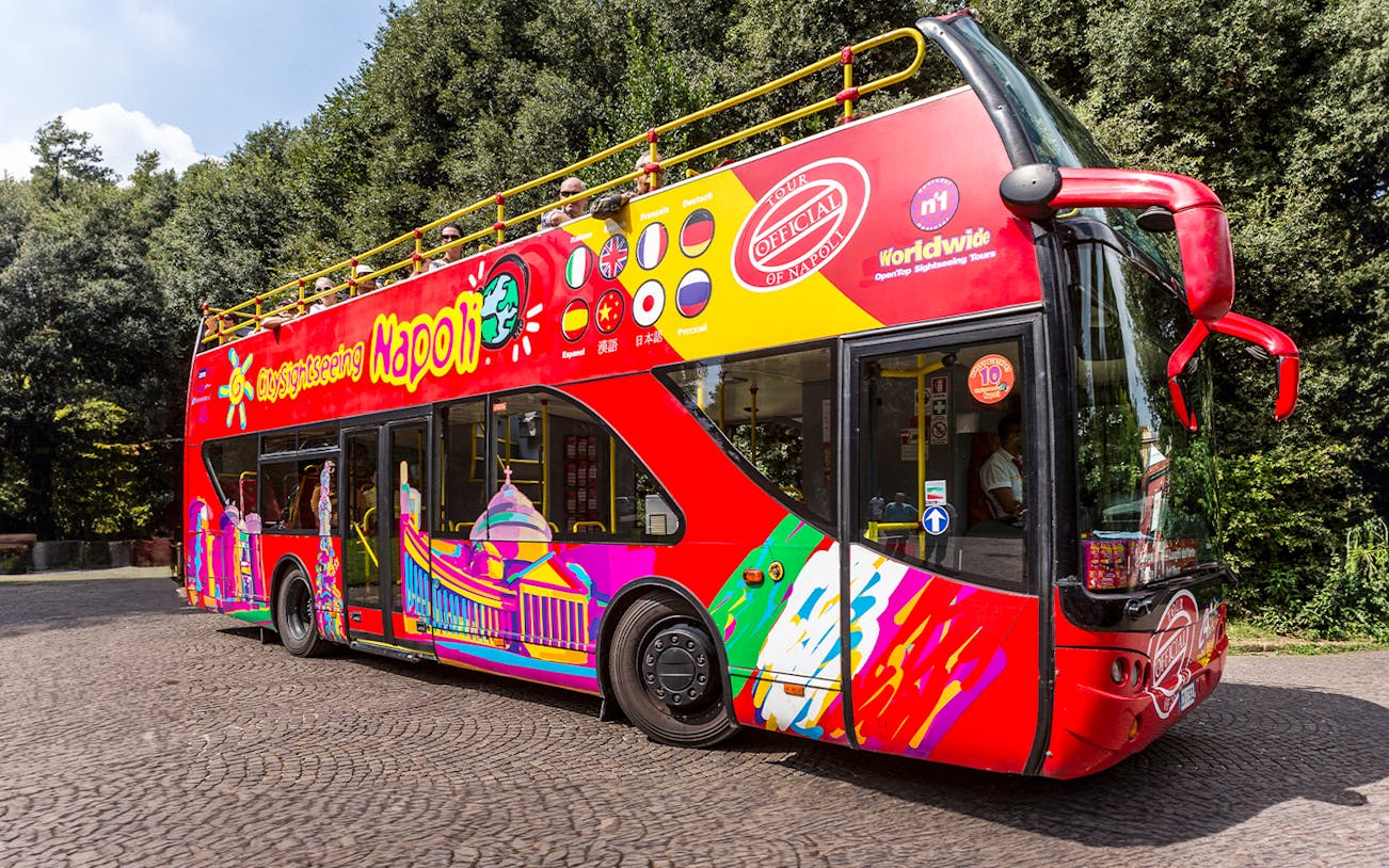 Red double-decker sightseeing bus in Naples with colorful designs and international flags.