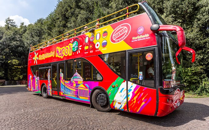 Red double-decker sightseeing bus in Naples with colorful designs and international flags.