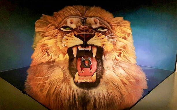 Person posing inside a 3D lion's mouth at Alive 3D Art Gallery.
