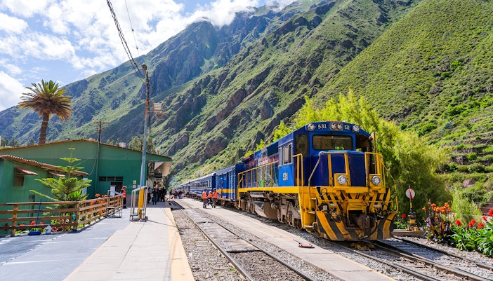 PeruRail train at station with Andes mountains in background, en route to Machu Picchu.