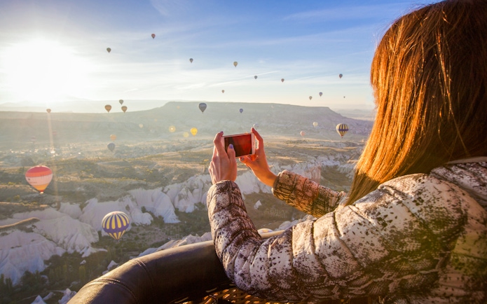 Person photographing Cappadocia landscape with hot air balloons in Turkey.