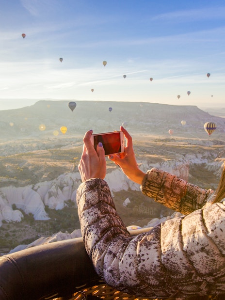 Person photographing Cappadocia landscape with hot air balloons in Turkey.