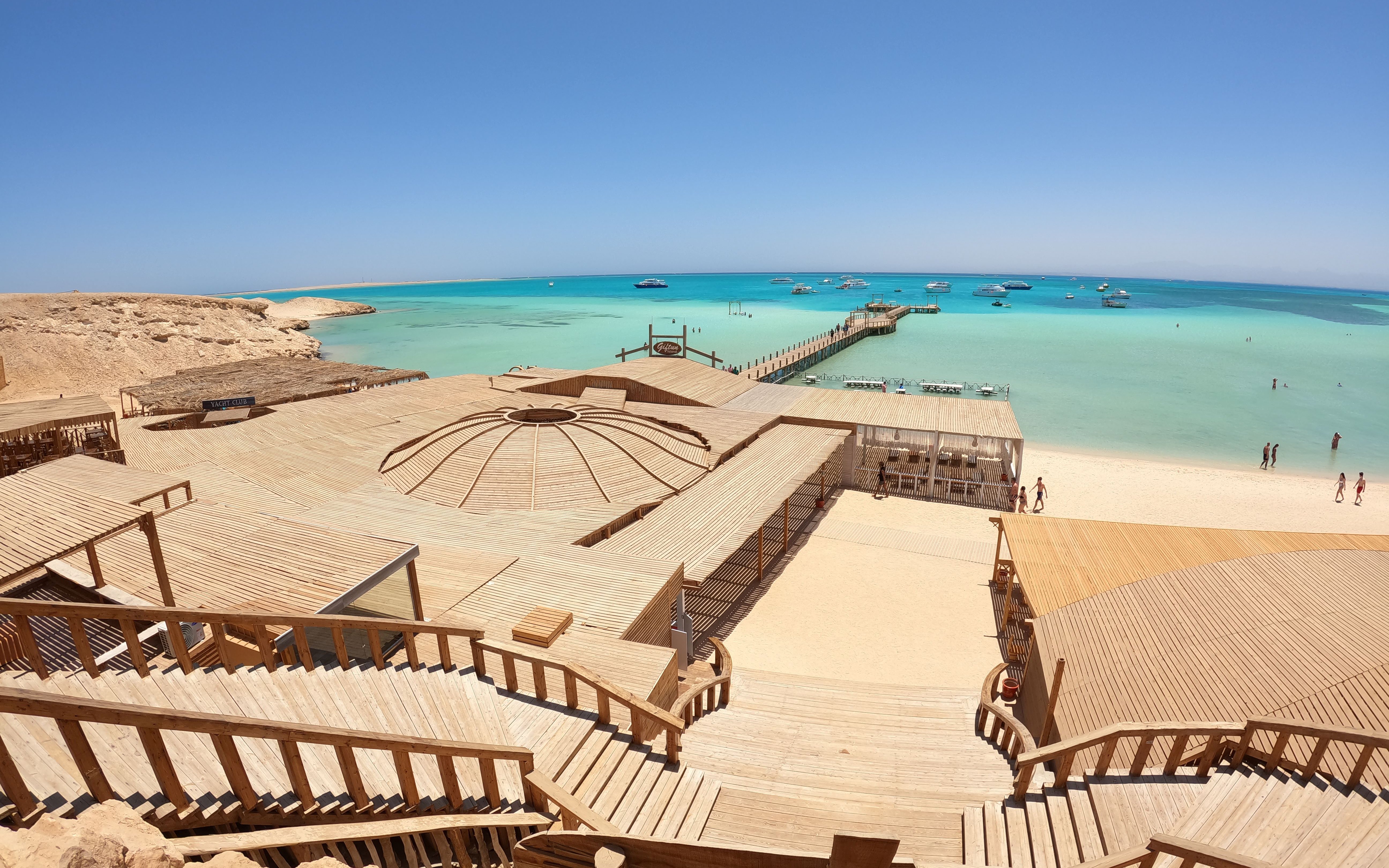 Deck and beach view of Orange Bay Island, Hurghada with turquoise sea and boats in the distance.