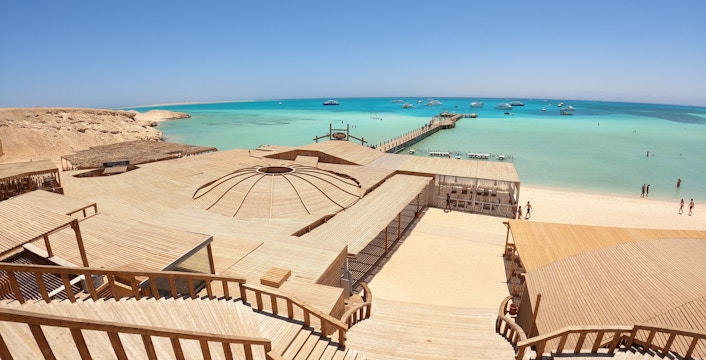 Deck and beach view of Orange Bay Island, Hurghada with turquoise sea and boats in the distance.