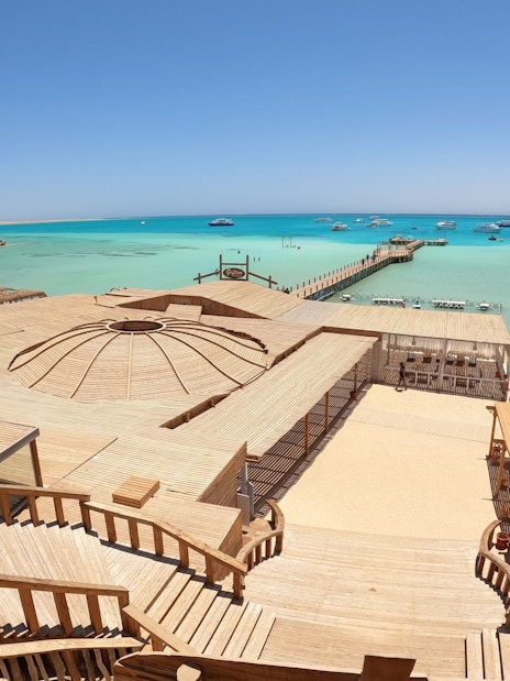 Deck and beach view of Orange Bay Island, Hurghada with turquoise sea and boats in the distance.