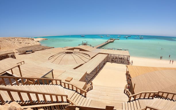 Deck and beach view of Orange Bay Island, Hurghada with turquoise sea and boats in the distance.