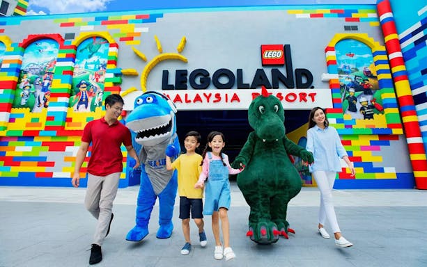 Visitors with mascots at LEGOLAND Malaysia entrance, vibrant LEGO-themed decor.